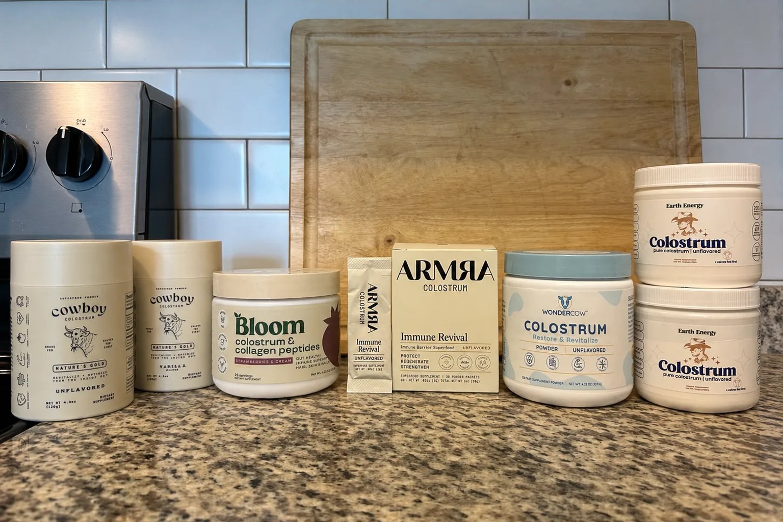 All the colostrum products we purchased for this comparison photographed together: Cowboy Colostrum unflavored and vanilla, Bloom colostrum and collagen, ARMRA Immune Revival, WonderCow, and two Earth Energy Colostrum jars