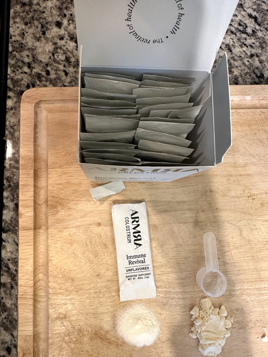 Opened ARMRA Immune Revival box showing 30 stick packets, with one packet face-up printing Net Wt .03 oz (1 g), next to a rival's scoop and powder piles for comparison