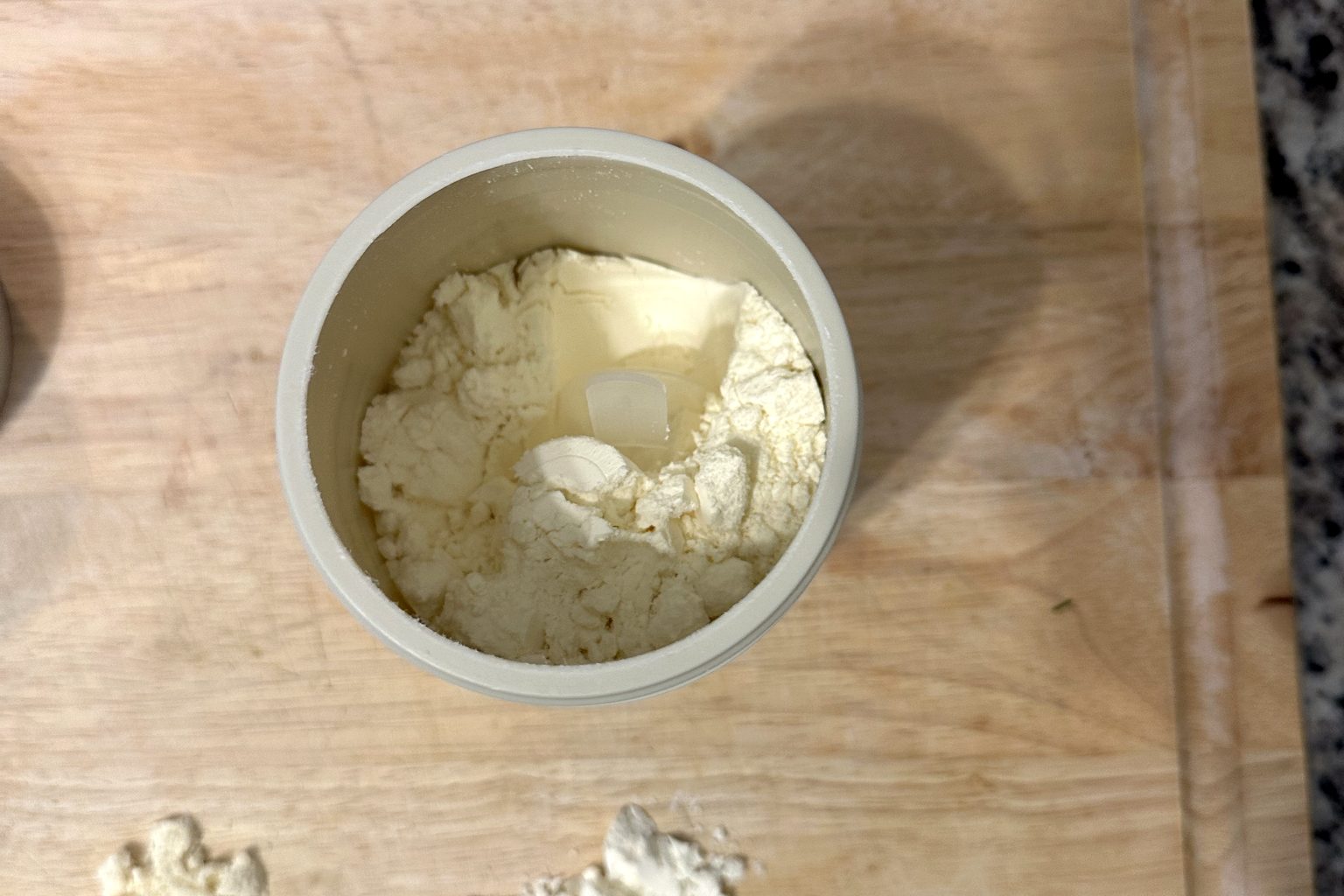 An open Cowboy Colostrum tube with its scoop and a pile of flaky pale-yellow colostrum powder on a cutting board