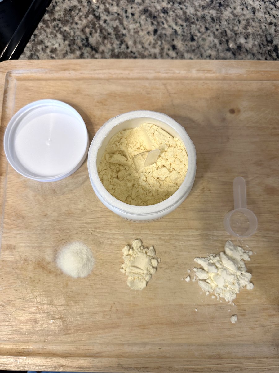 Opened Earth Energy Colostrum jar showing pale-yellow powder with scoop, next to powder piles from rival colostrum products on a cutting board