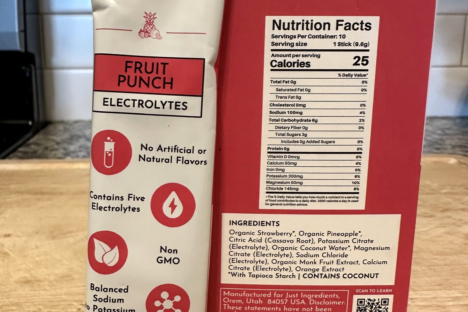 Just Ingredients Fruit Punch Electrolytes stick pack next to the box's Nutrition Facts panel showing 100 mg sodium and 300 mg potassium per stick